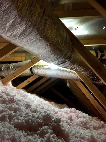A bunch of pipes are hanging from the ceiling of an attic.