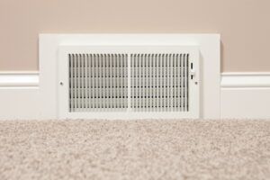 A white air vent is sitting on a carpeted floor next to a wall.