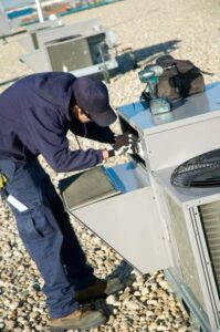 A man is working on an air conditioner on the roof of a building.