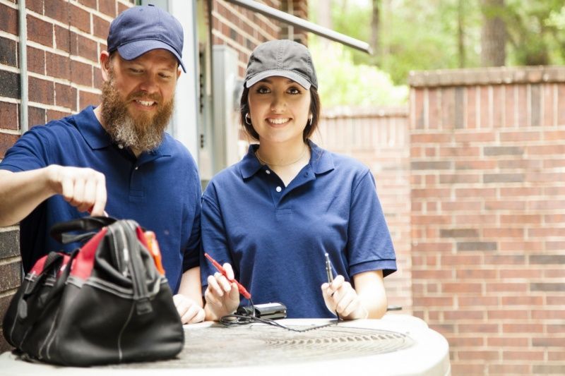 A man and a woman are working on an air conditioner.