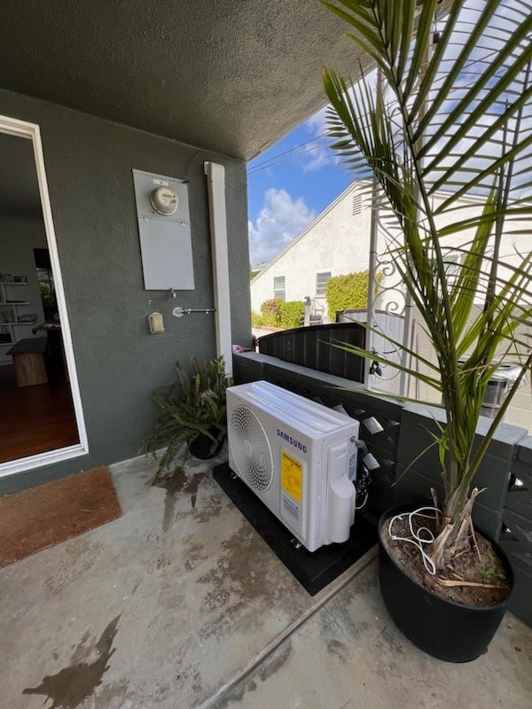 A panasonic air conditioner is sitting on a balcony next to a potted plant.