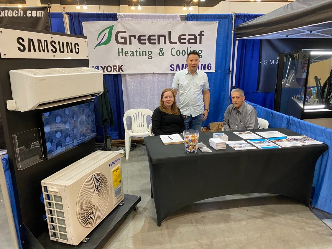 A group of people are sitting at a table in front of a samsung air conditioner.