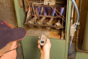 A man is holding a remote control in front of a furnace.