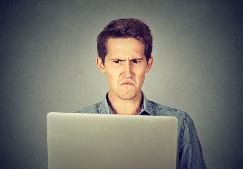 A man is making a funny face while using a laptop computer.