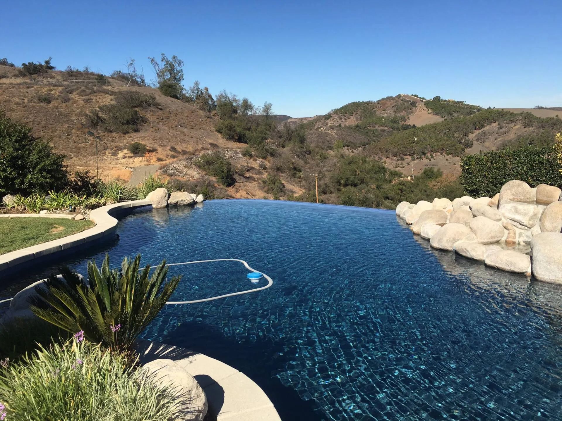 Infinity pool overlooking rolling hills, blue water, sunny day.