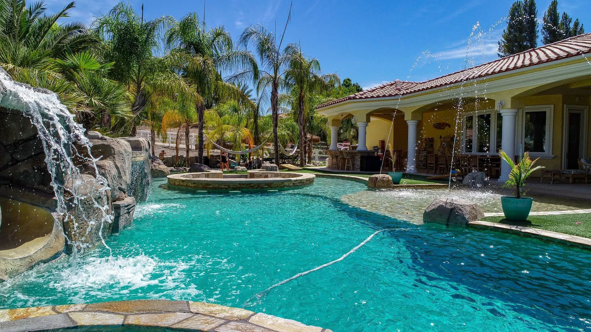 Luxury backyard pool with waterfall, palm trees, and outdoor living space.