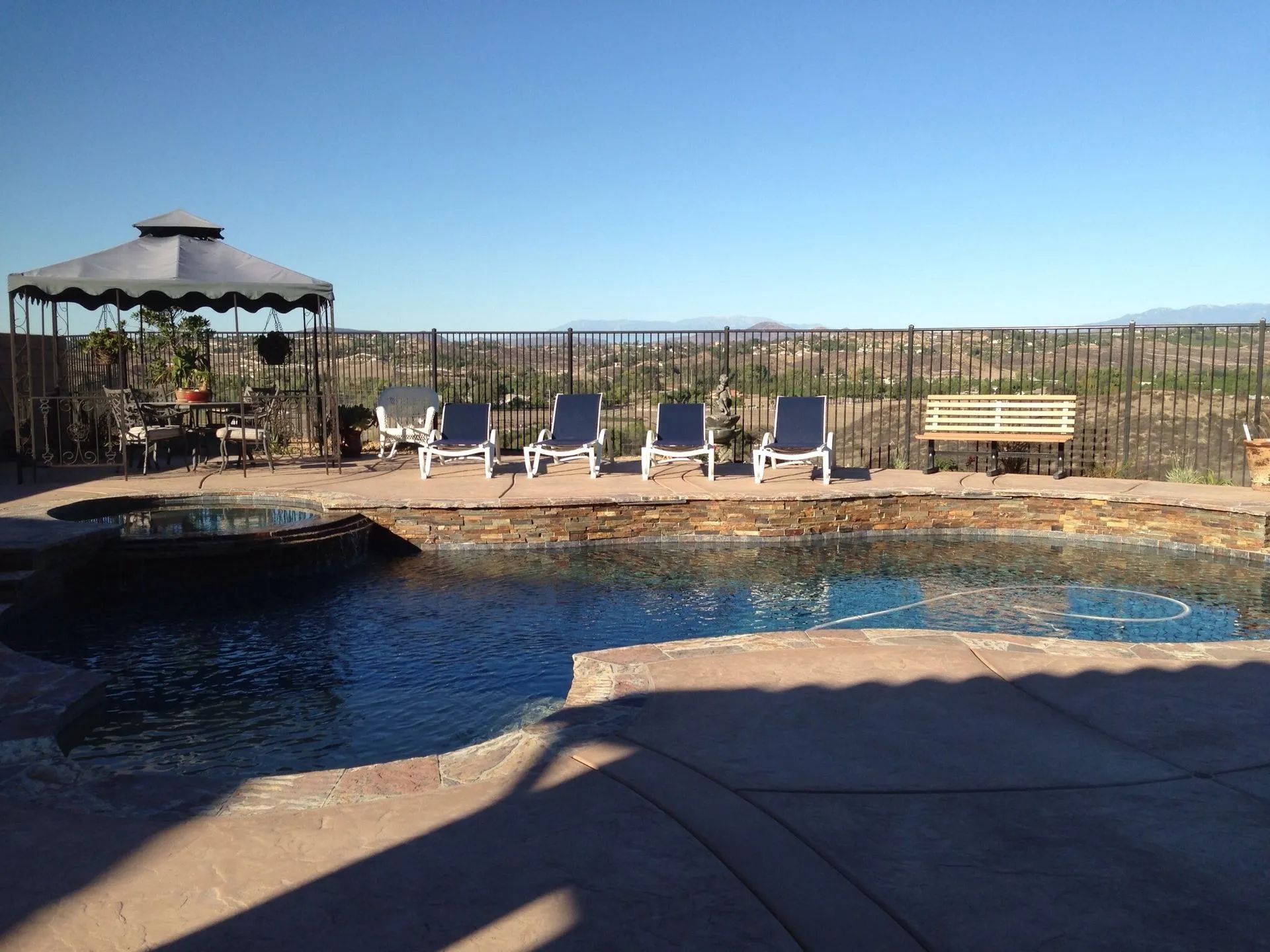 Pool with lounge chairs, a gazebo, and a bench overlooking a desert landscape under a clear blue sky.