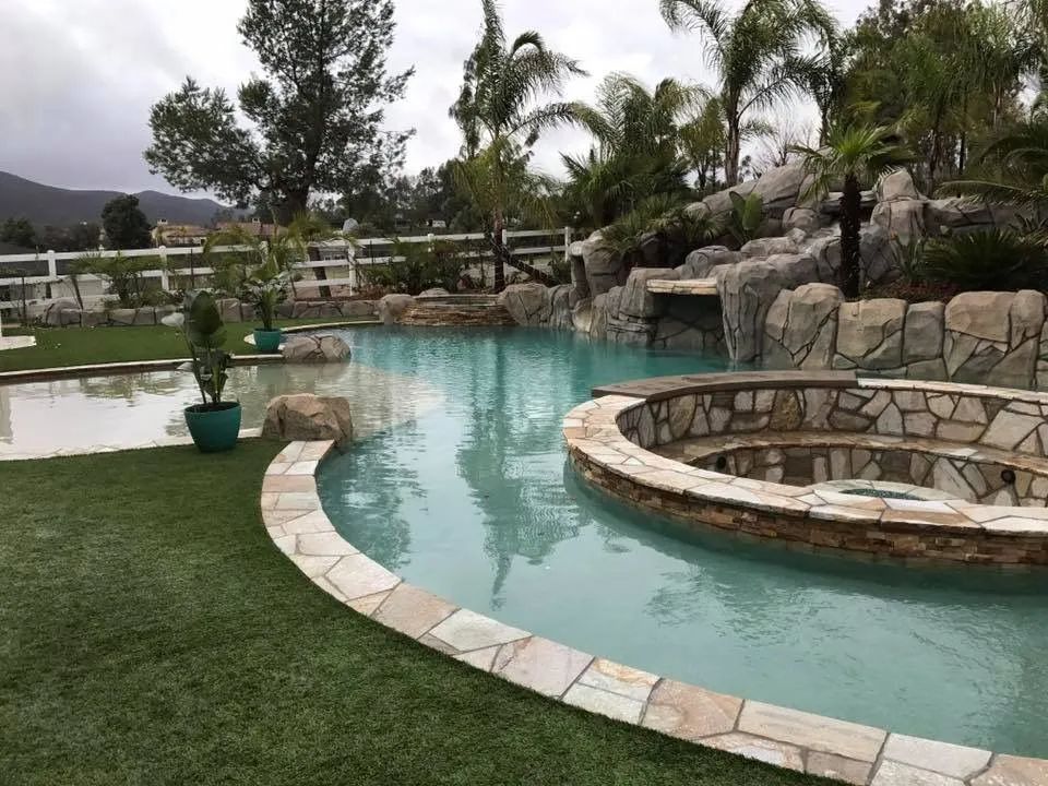 Luxurious pool with waterfall and hot tub, surrounded by green grass and stone accents.