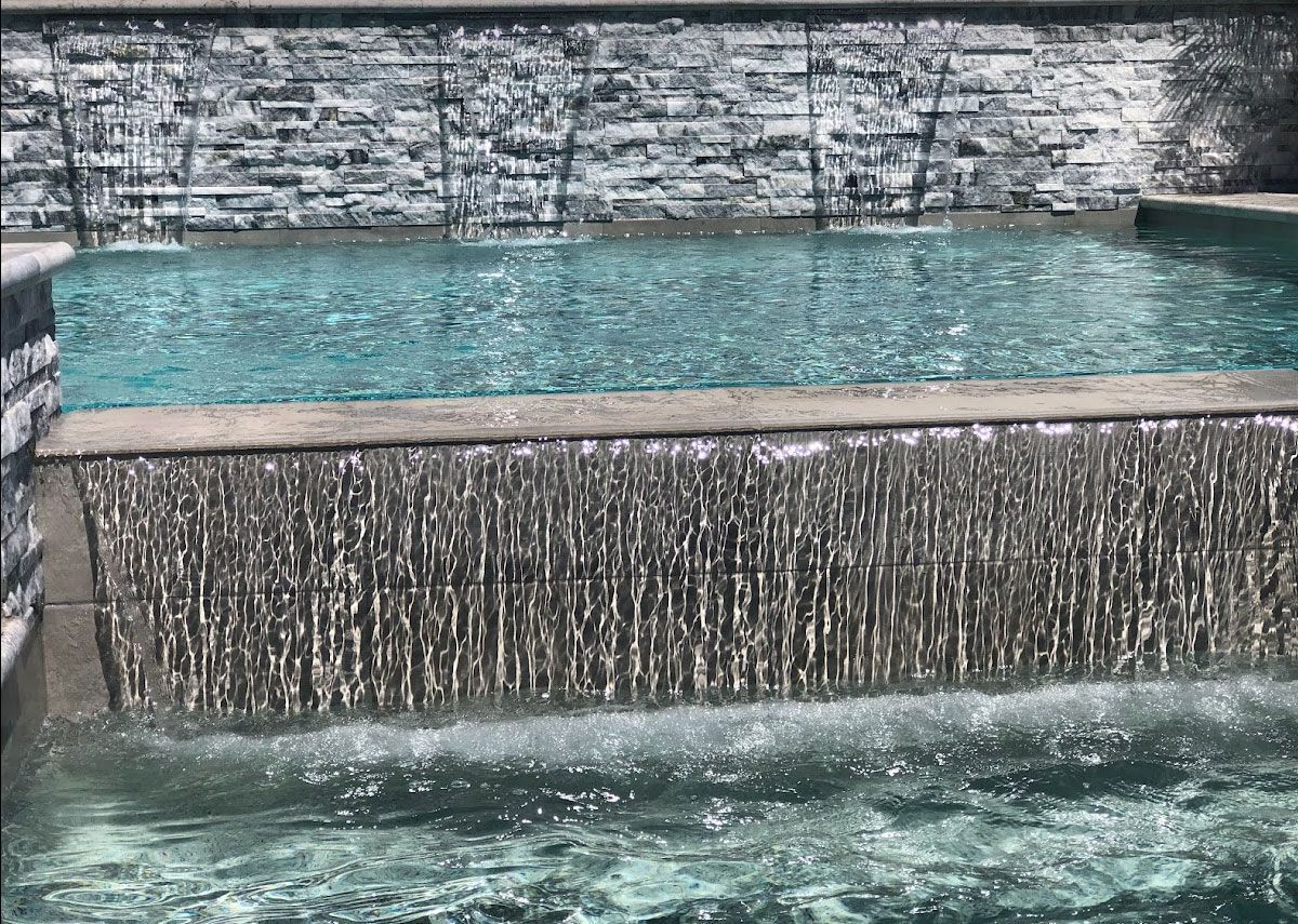 Water cascading from a stone-textured wall into a turquoise pool.