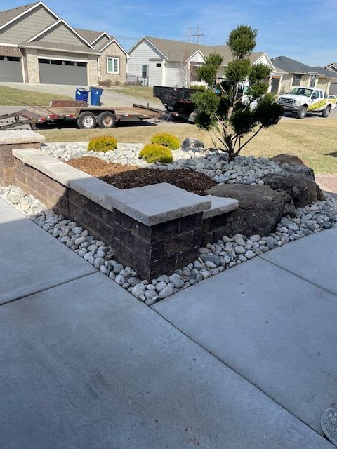 Landscaped front yard with brick retaining wall, rocks, and small evergreen tree.