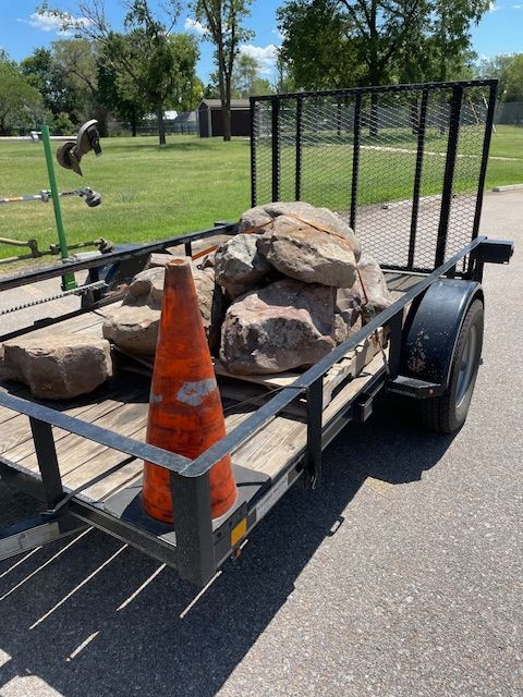 Trailer loaded with rocks and a traffic cone, on an asphalt surface.