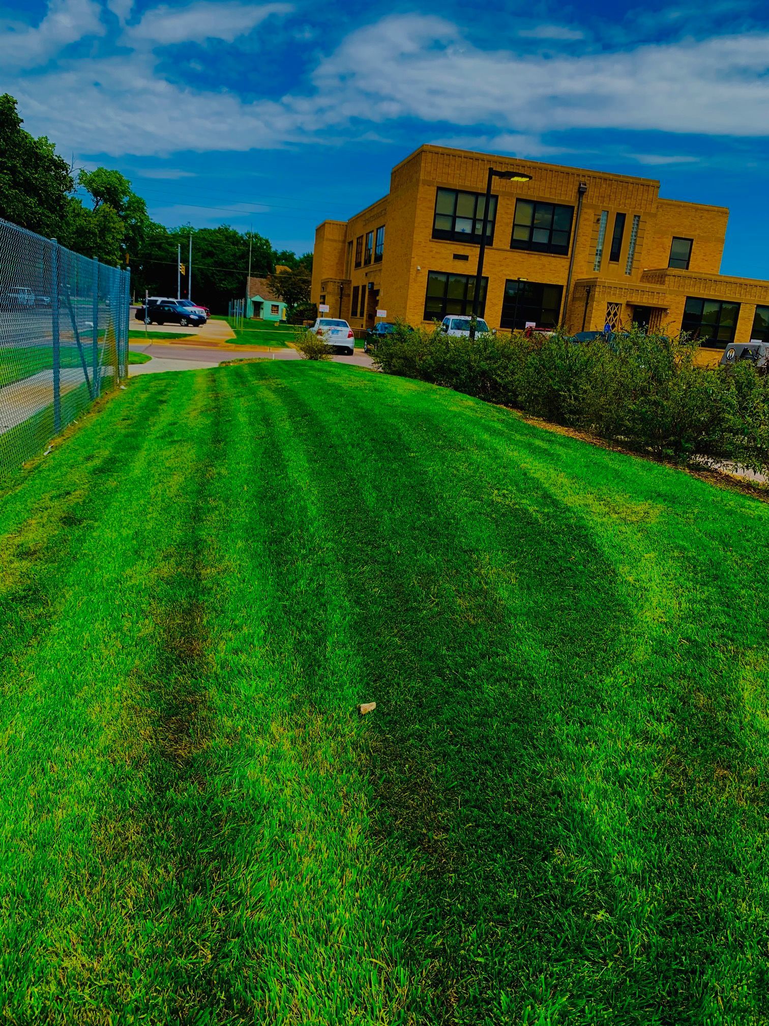 Lush green lawn in front of a yellow brick building on a sunny day with blue sky.