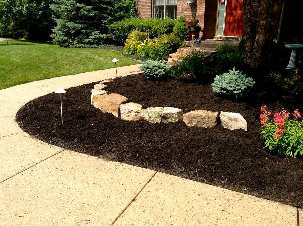 Curving walkway beside a flower bed edged with large rocks and fresh dark mulch.