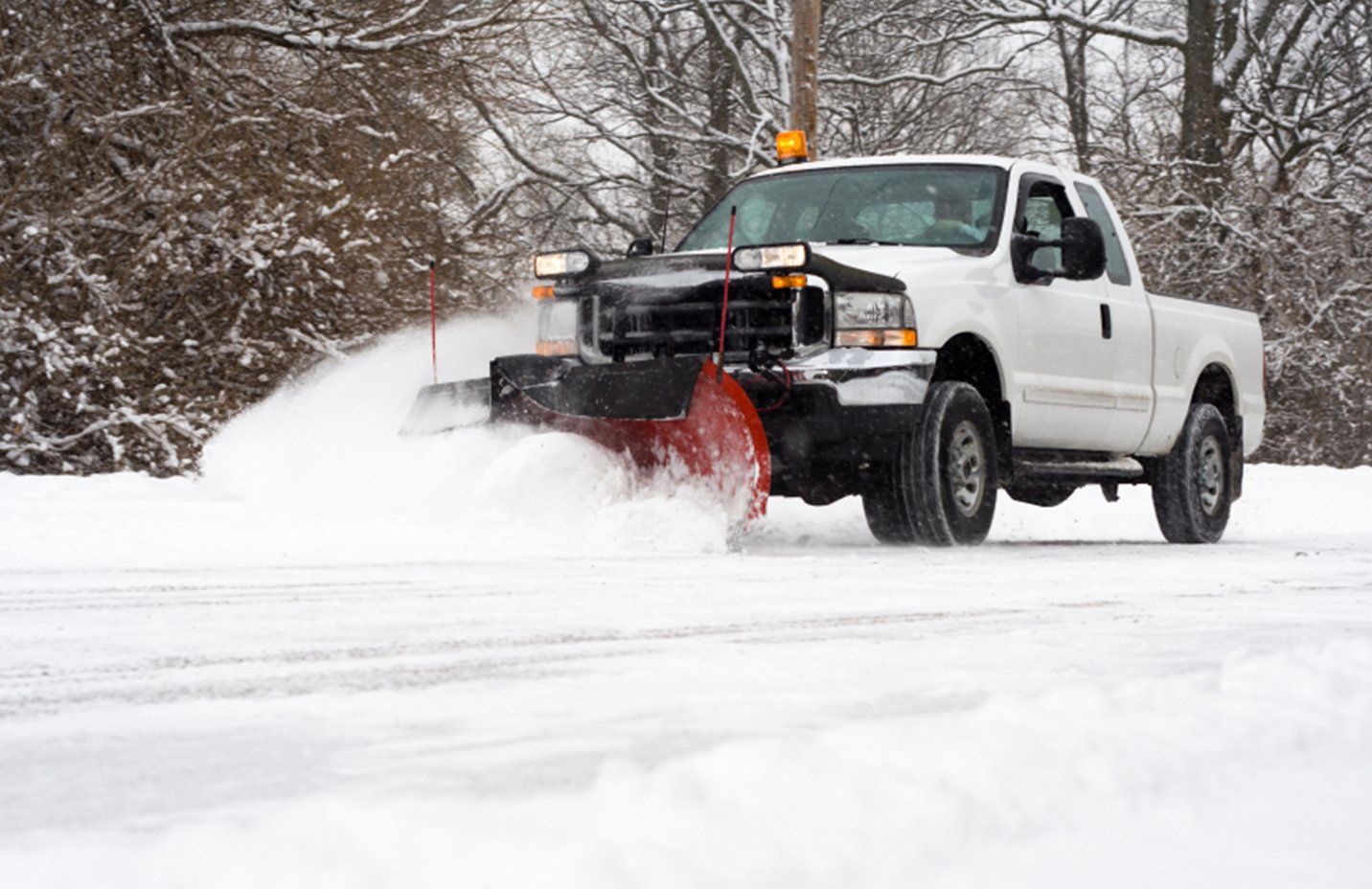White truck with plow clearing snow from a road in a snowy environment.