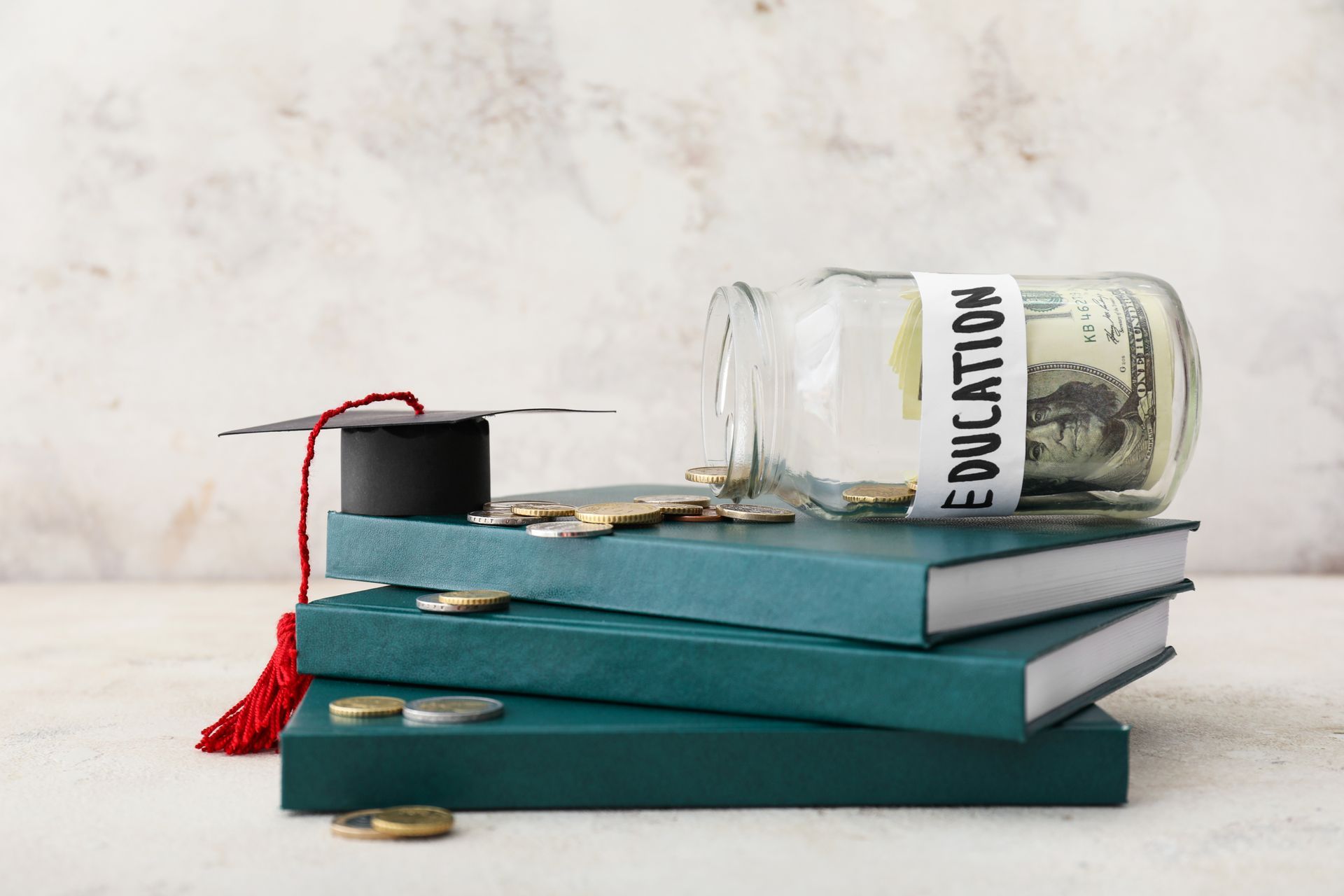 A stack of books with a graduation cap and a jar of money on top of them.