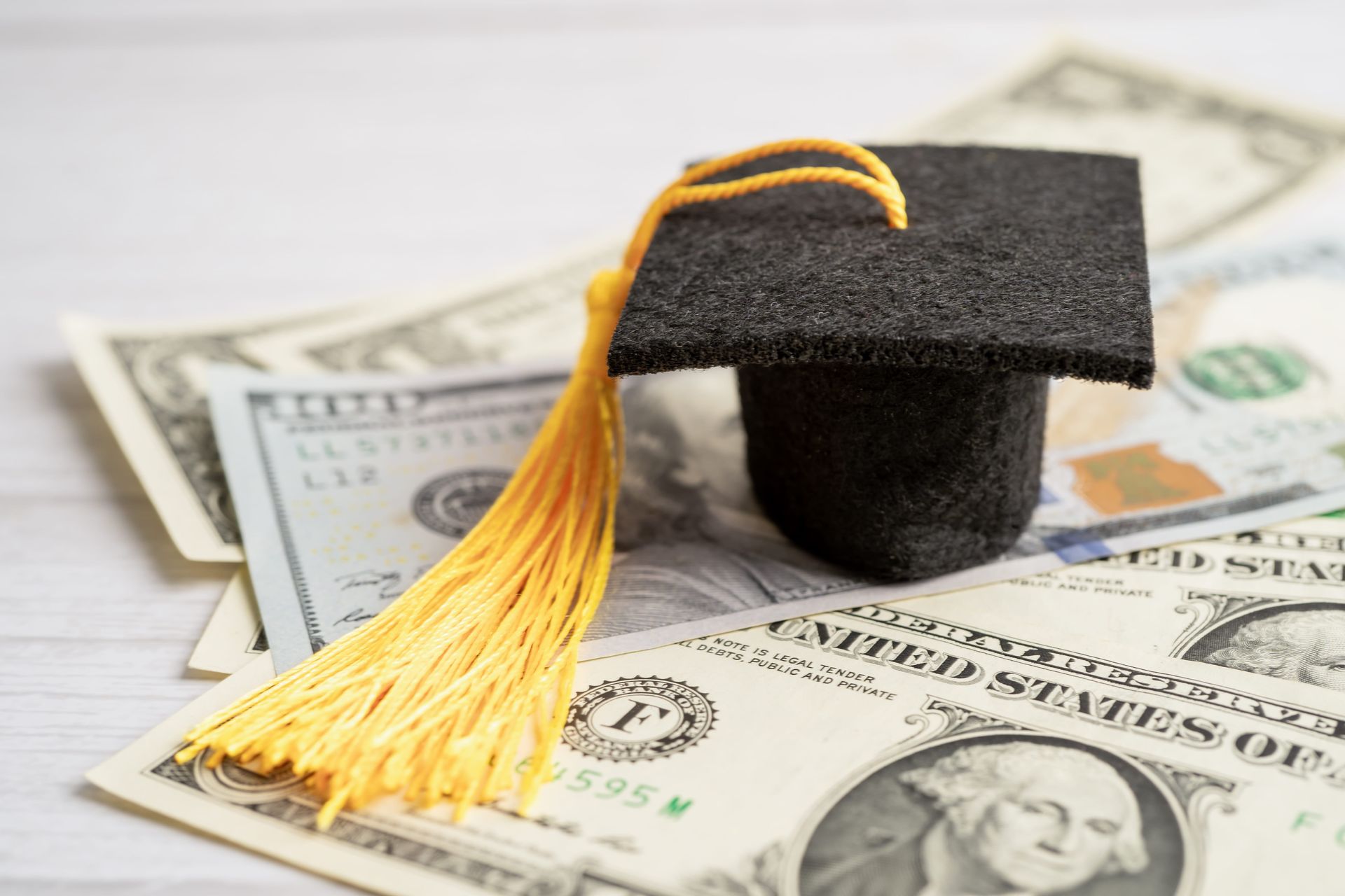 Graduation cap on U.S. dollar bills, symbolizing education costs or student debt