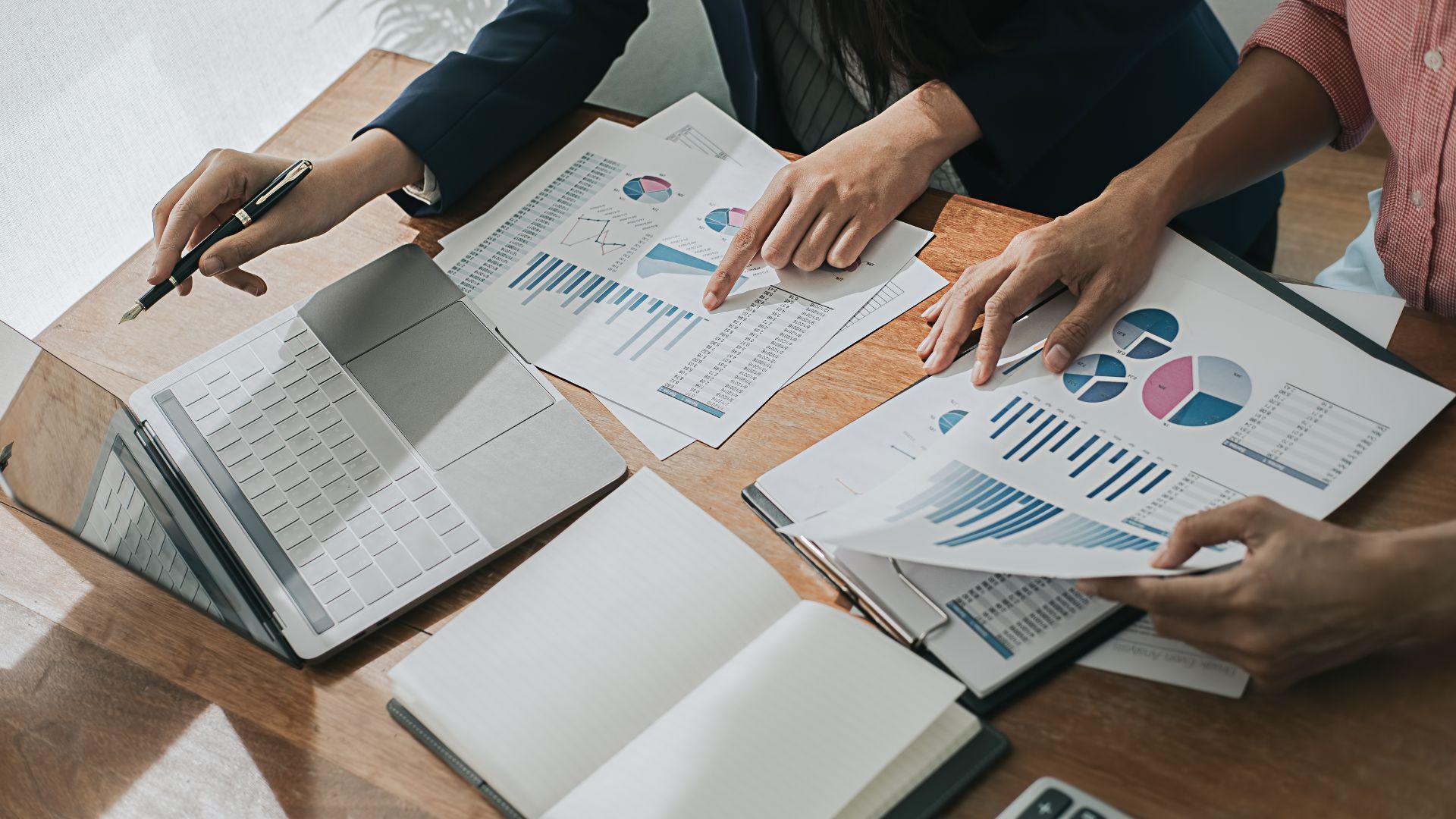 Two people reviewing business reports with charts and graphs, at a desk.