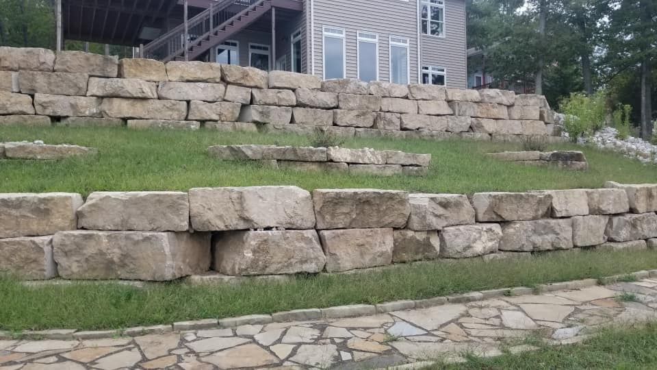 Stone retaining walls tiered on a grassy hillside in front of a multi-story building with large windows.