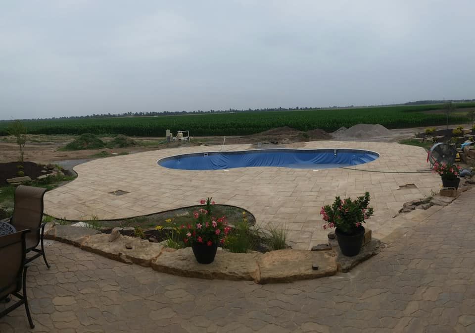 A partially constructed pool with a blue tarp cover surrounded by stone paving.