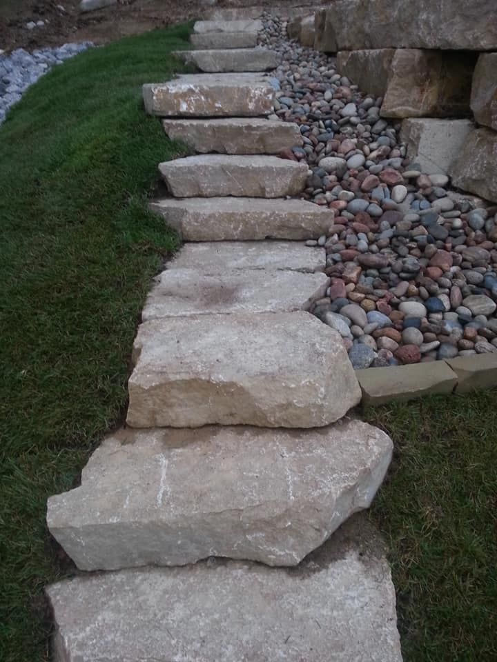 Stone steps leading up a grassy slope, with a bed of colorful pebbles to the side.