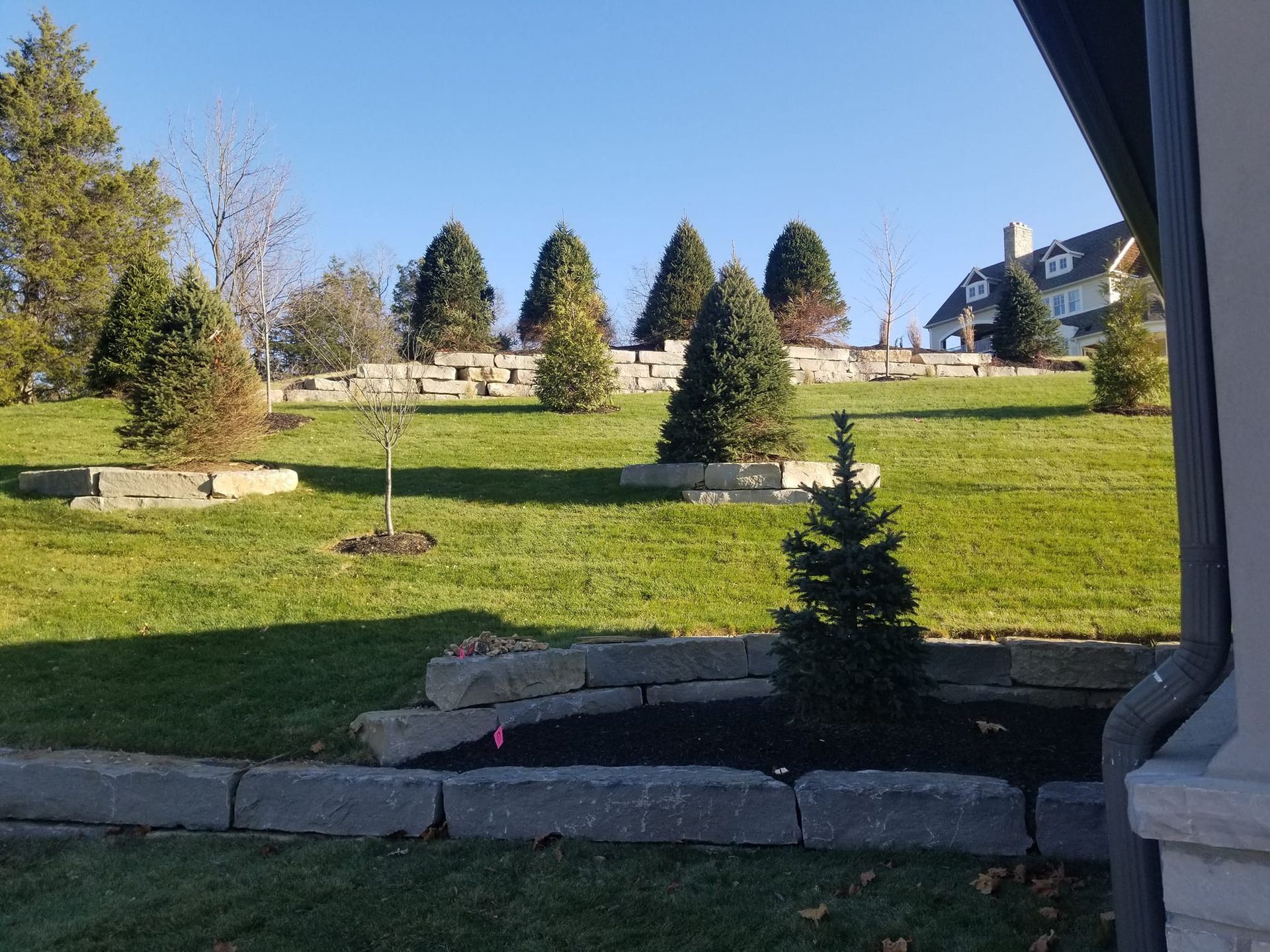 A sunny grassy hillside with tiered stone retaining walls.