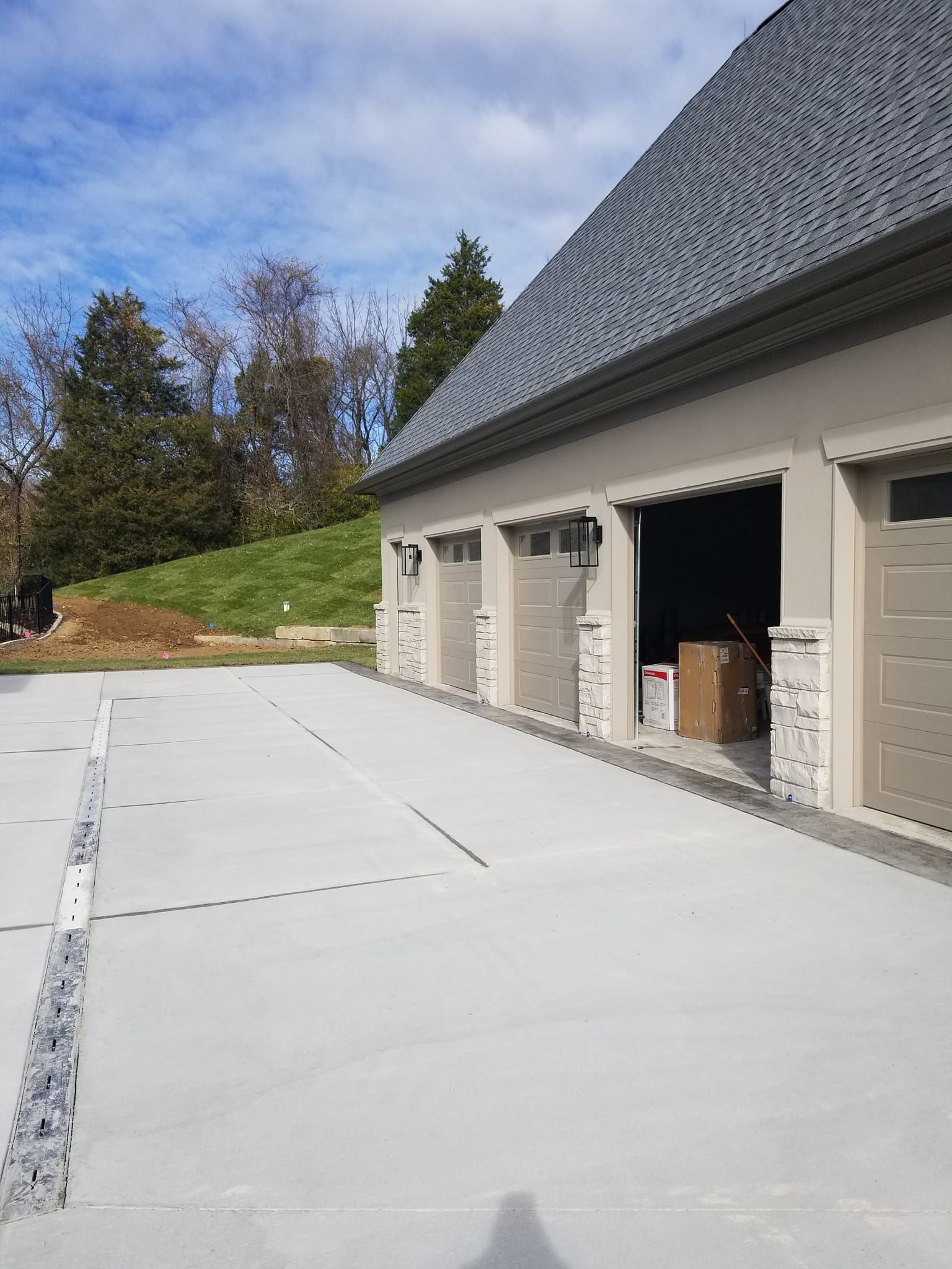 A concrete driveway leads to a three-car garage with gray doors. The garage is beige and has a gray roof.