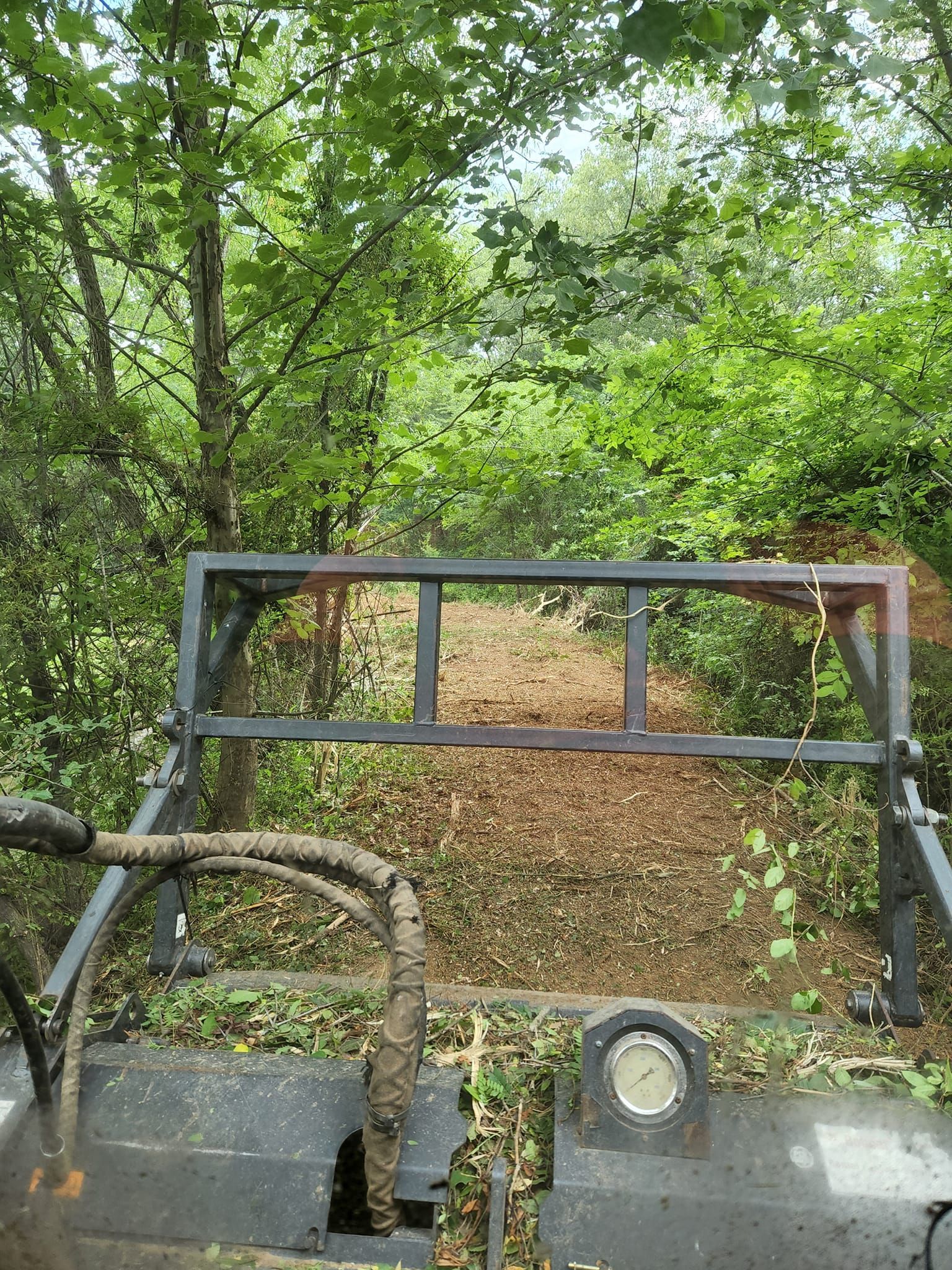A forward-facing view from inside heavy machinery, looking through a metal grate at a wood-chipped trail.