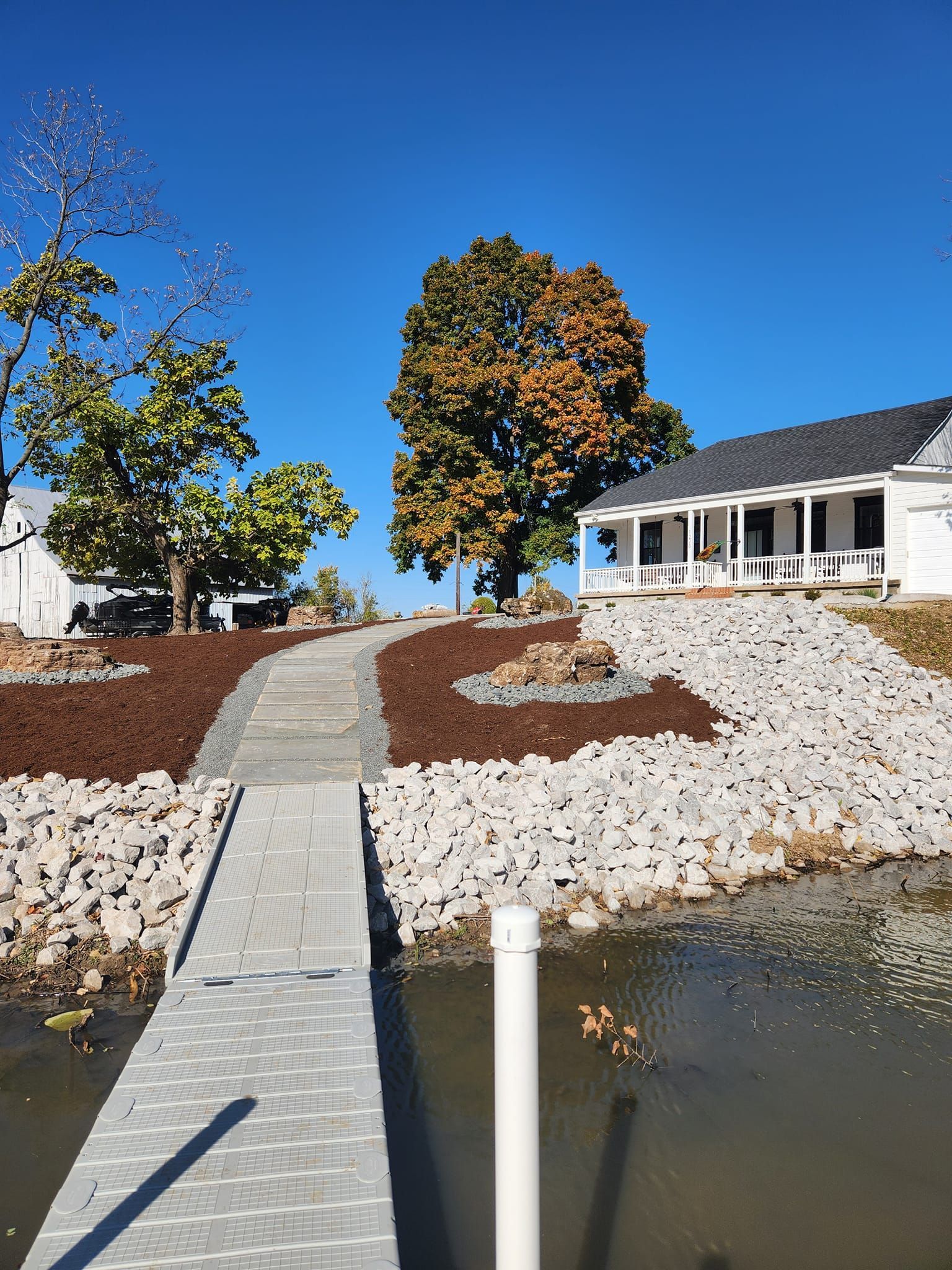 A white house with a porch sits by a body of water, connected by a gray pathway.