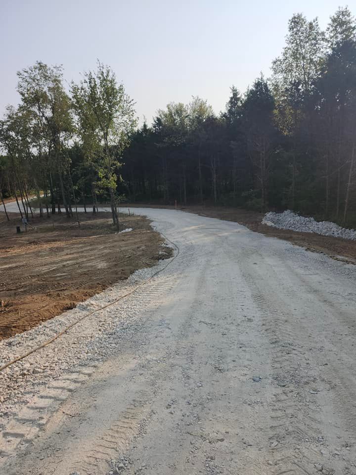 Gravel road curves through a clearing bordered by trees. The sky is light blue.