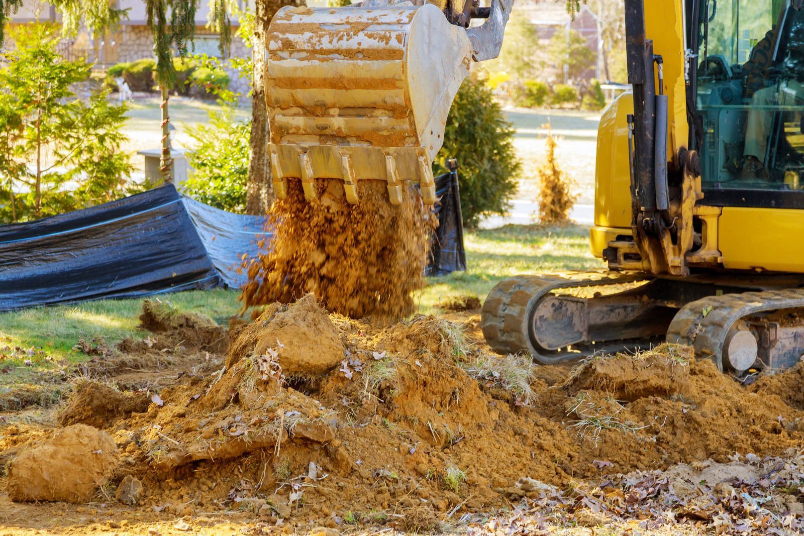 Yellow excavator digging dirt in a yard. The bucket is filled with soil, creating a small pile.