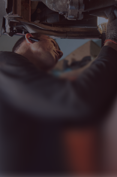 Mechanic working on the underside of a vehicle. Wearing gloves, looking up, indoors.