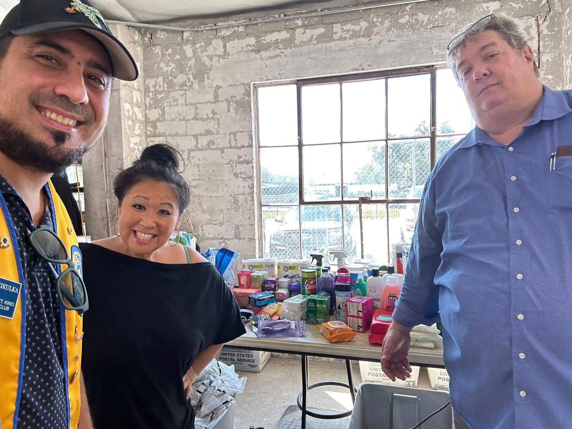 Three people smile near a table with supplies in a brightly lit room.