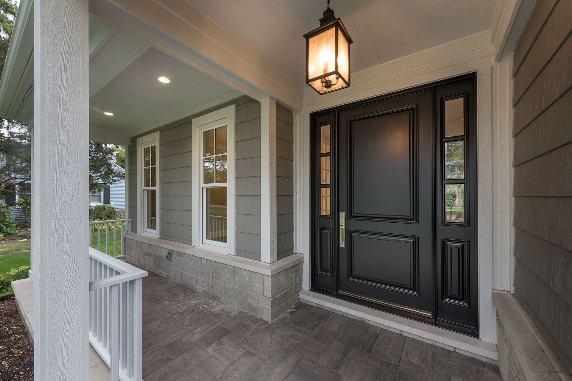 A porch with a black door and a lantern hanging from the ceiling.