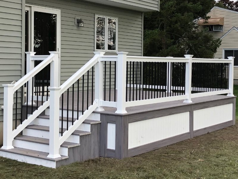A deck with stairs and a white railing is in front of a house.