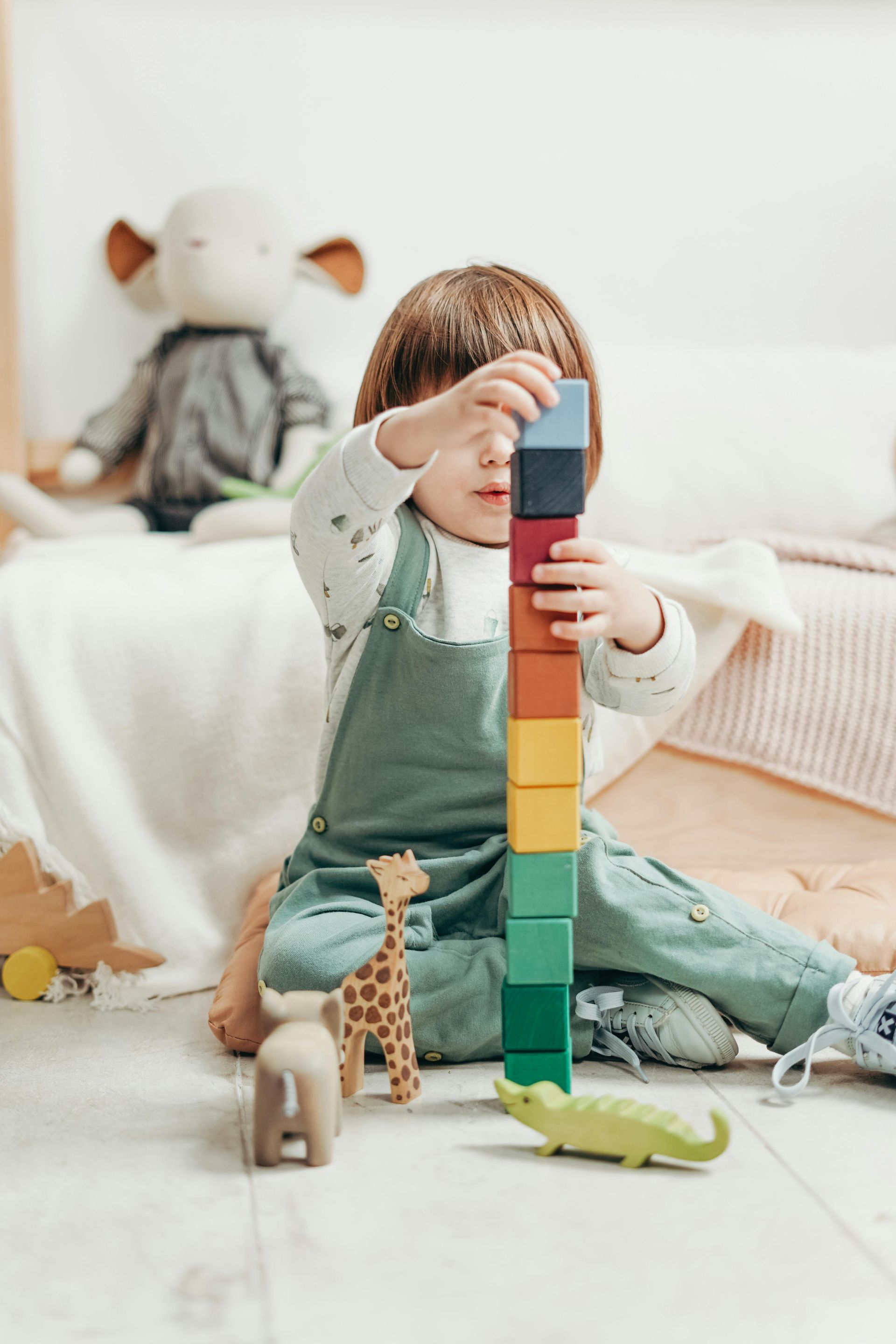 Child stacking colorful wooden blocks, surrounded by toys, indoors.