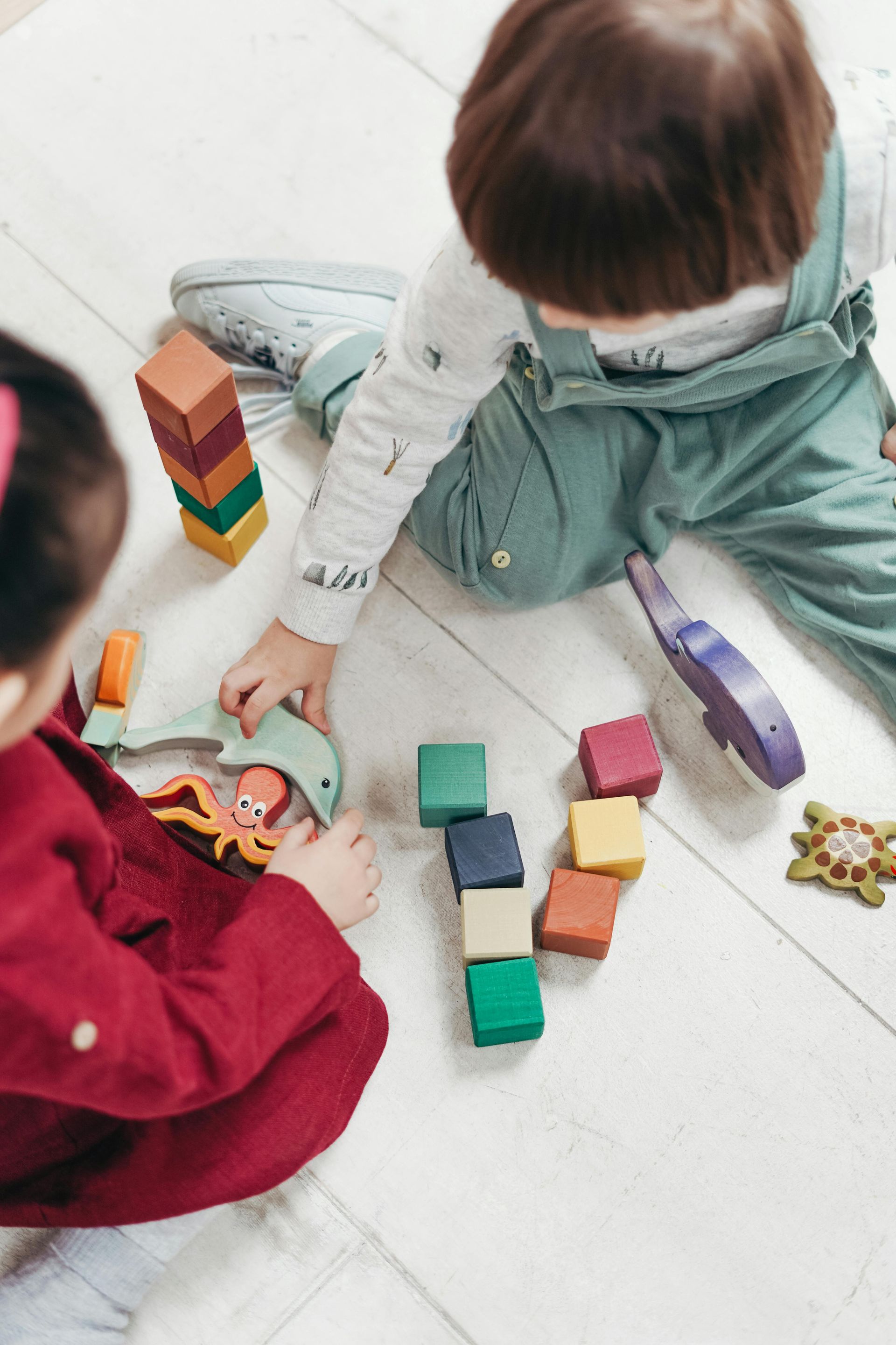 Two children playing with wooden blocks on a light wood floor.
