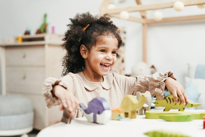 Girl with curly hair laughs while playing with colorful wooden toys.