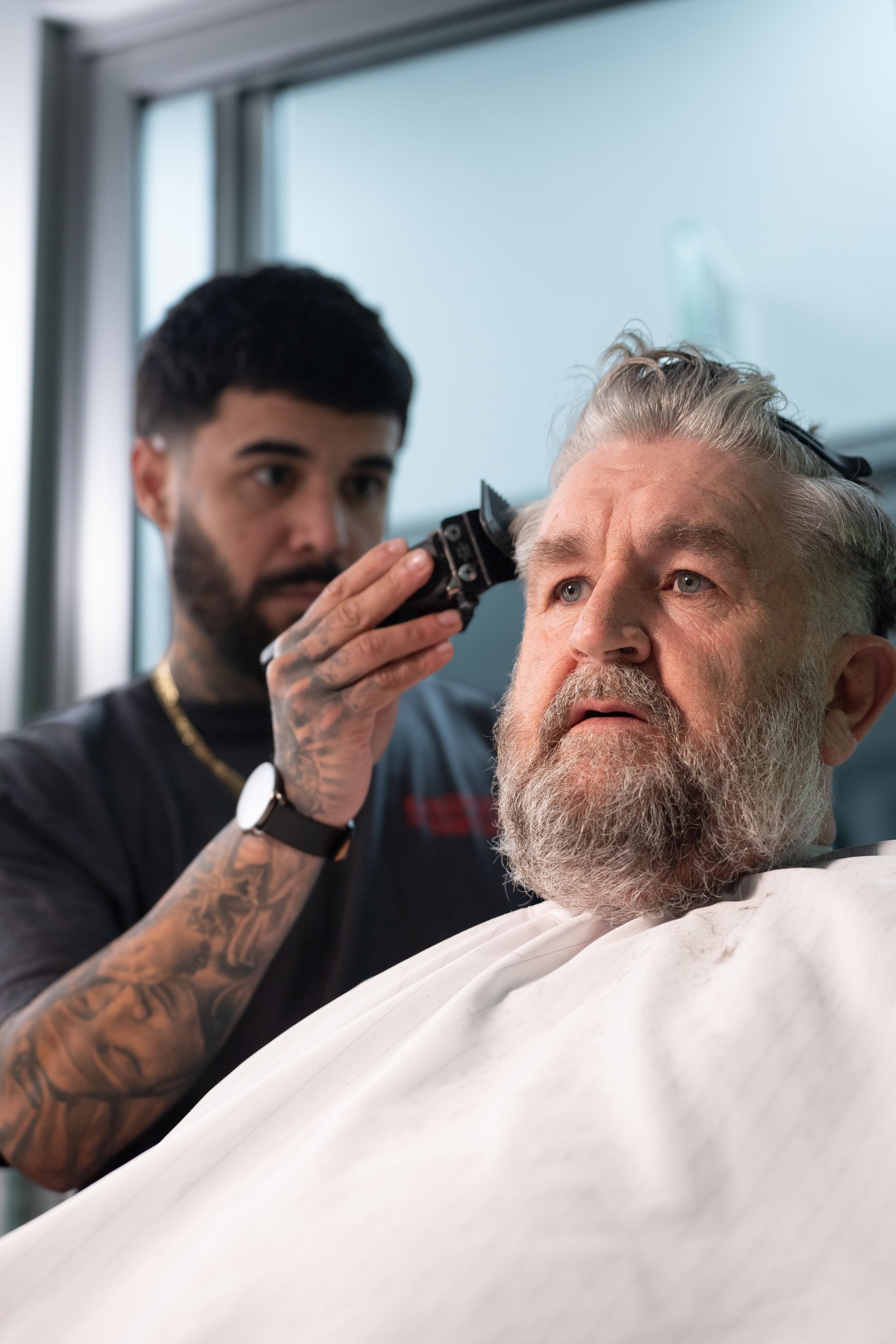 Barber using clippers on a customer's hair. The customer is seated, wearing a barber cape.