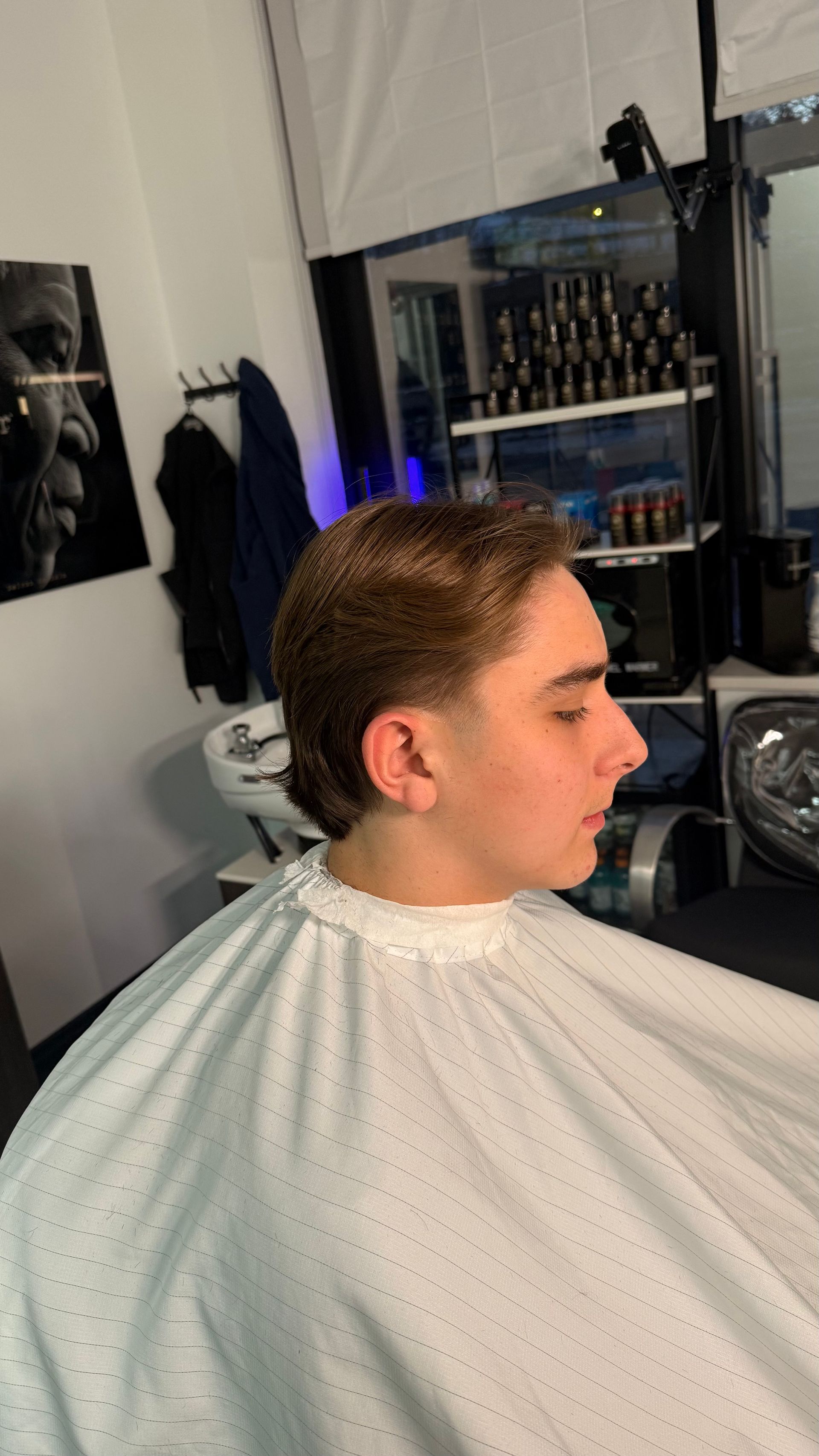 A person with a new haircut wearing a salon cape, in a barber shop setting.