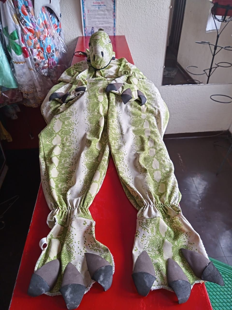 Un disfraz de dinosaurio verde y blanco está sobre una mesa roja.