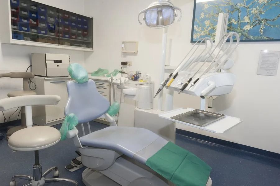 Poltrona odontoiatrica in uno studio pulito con attrezzature mediche, pareti blu e un dipinto.