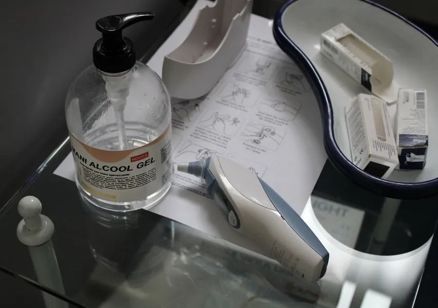 Tavolo in vetro trasparente con disinfettante per le mani, materiale medico, termometro e una bacinella in porcellana bianca.