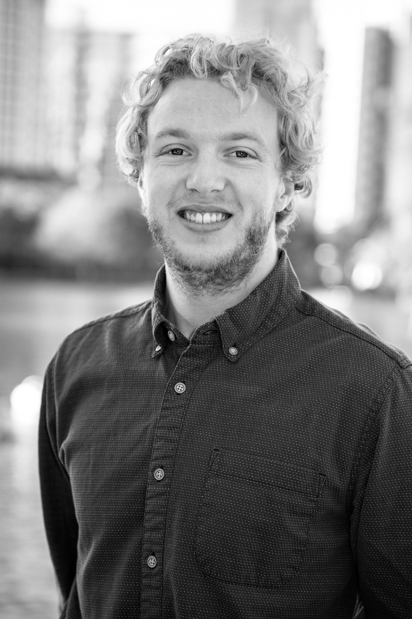 A man with curly hair and a beard is smiling in a black and white photo.
