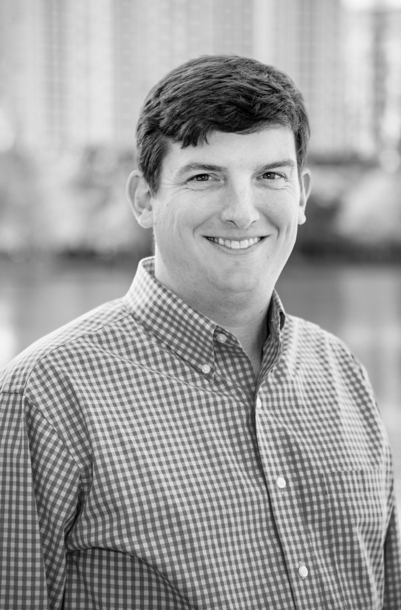 A man in a plaid shirt is smiling in a black and white photo.