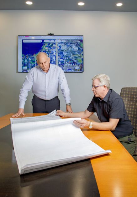 Two men are sitting at a table looking at a large piece of paper.