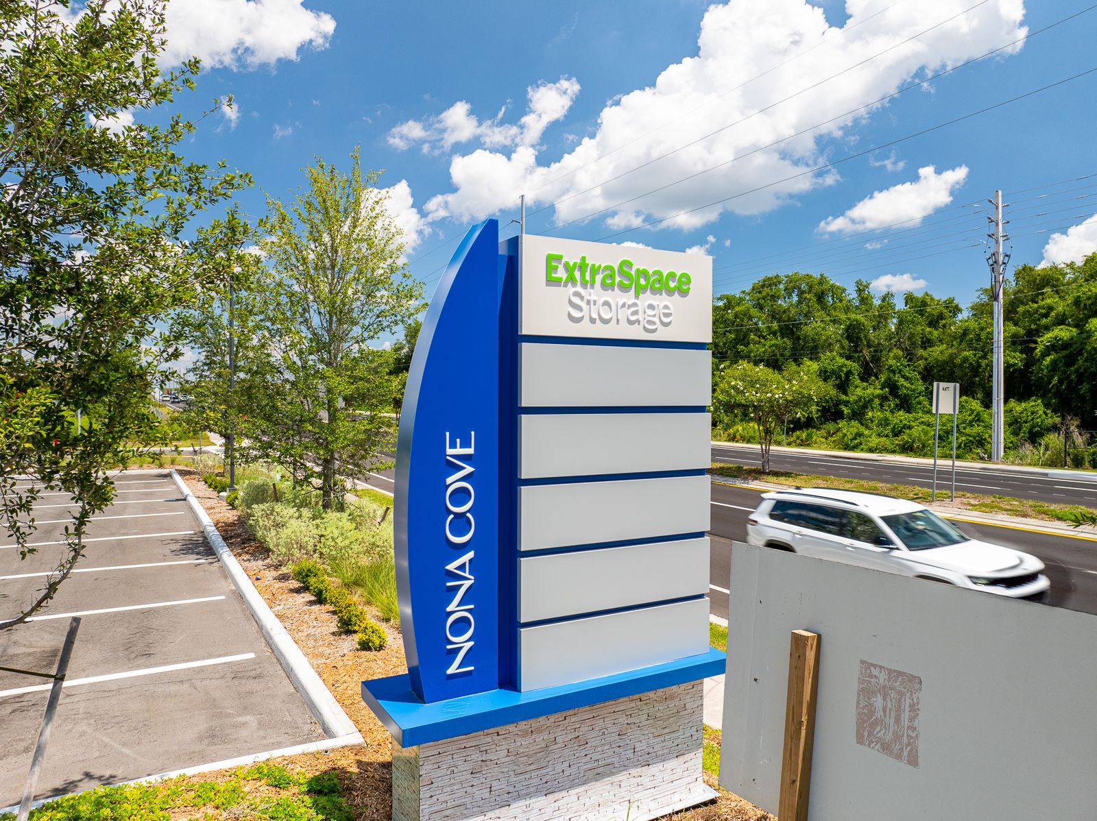 A blue and white sign for extra space storage is in front of a parking lot.