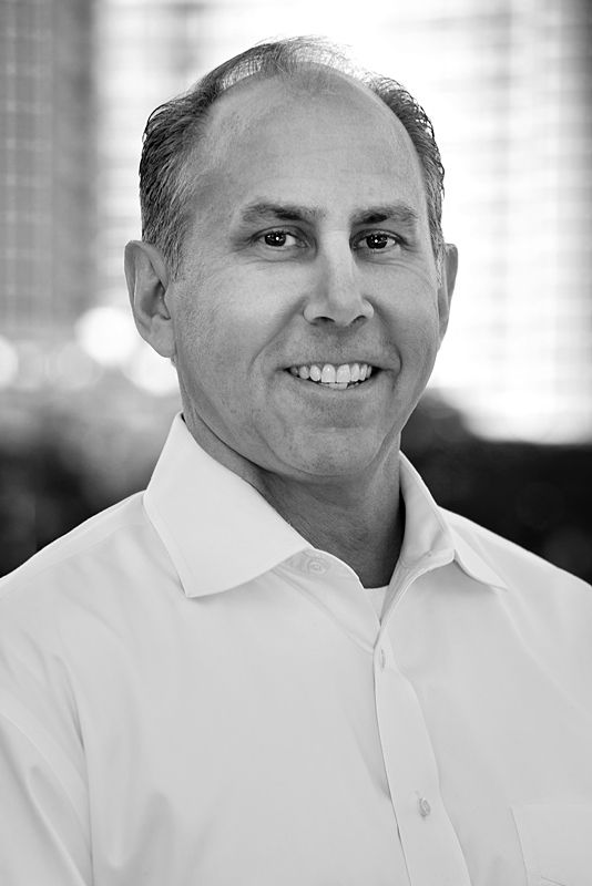 A man in a white shirt is smiling in a black and white photo.