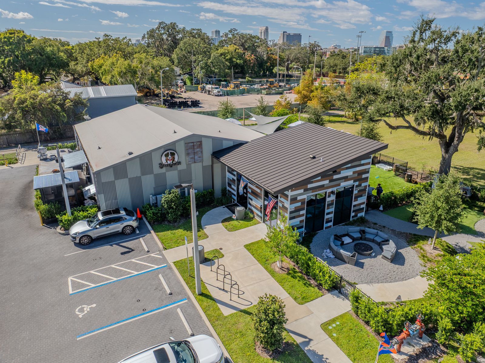Aerial view of a weathered metal building with a parking lot and a fire pit in a park-like setting.