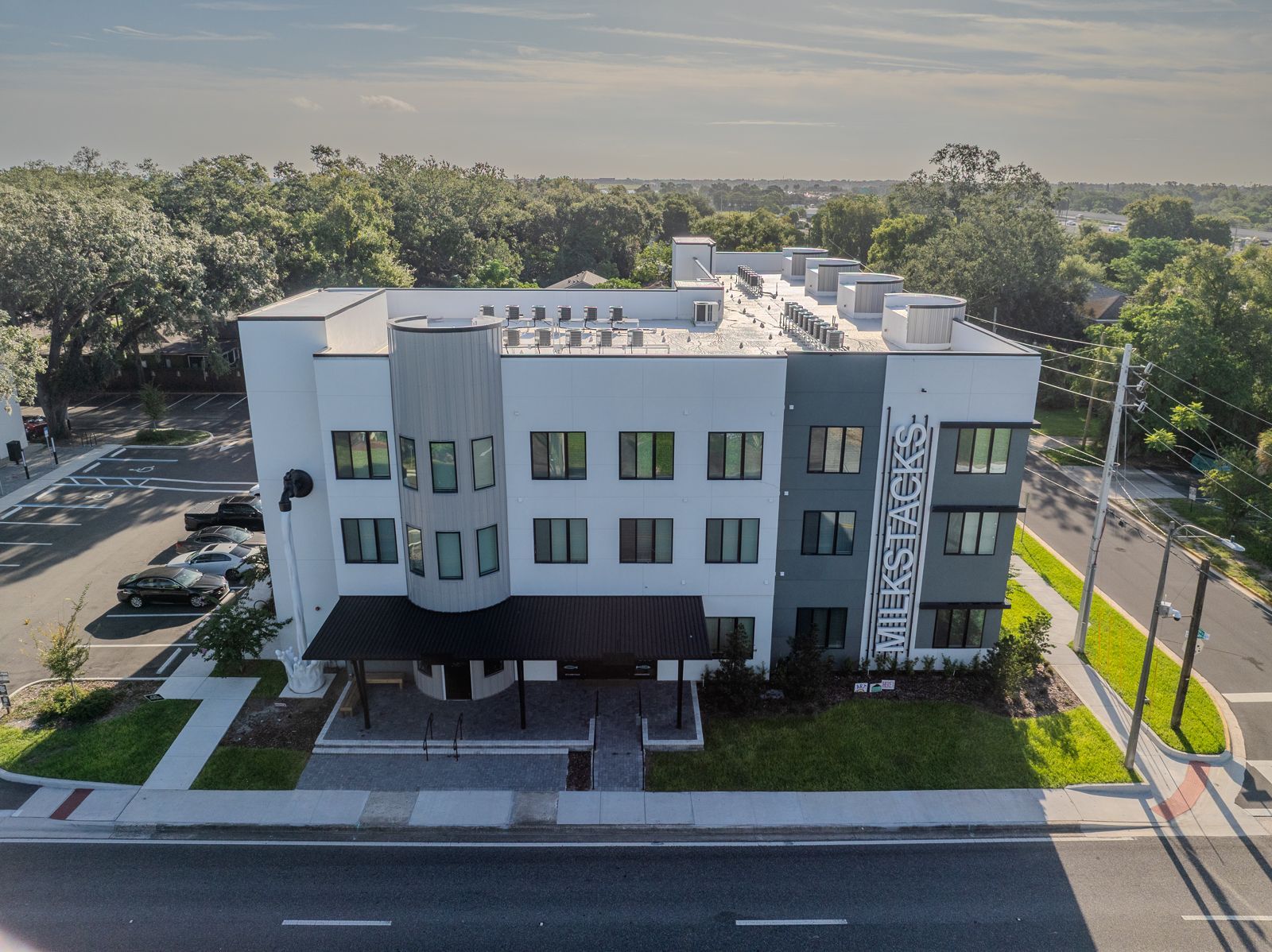 Modern three-story building with gray, white, and teal accents; trees in the background.