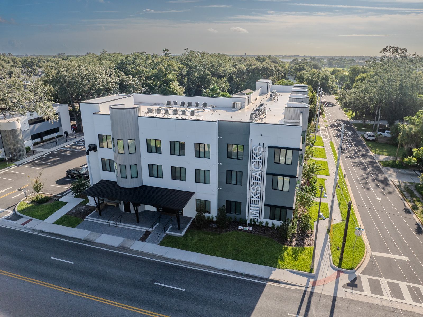 Modern multi-story building with a black awning on a sunny street, surrounded by trees.